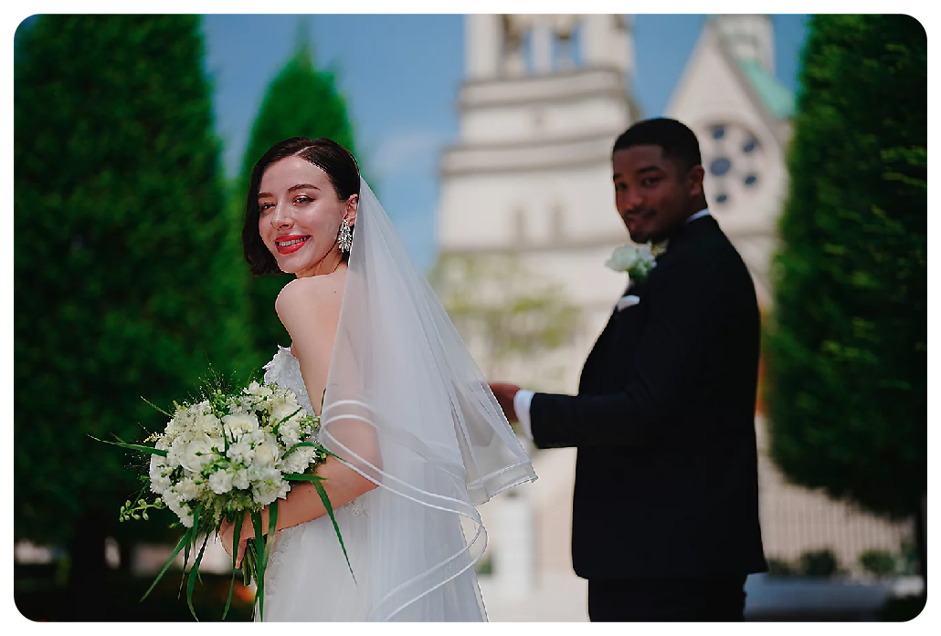 Sony A7 IV sample image of married couple standing in wedding dress and black tuxedo infront of gothic style church in the background